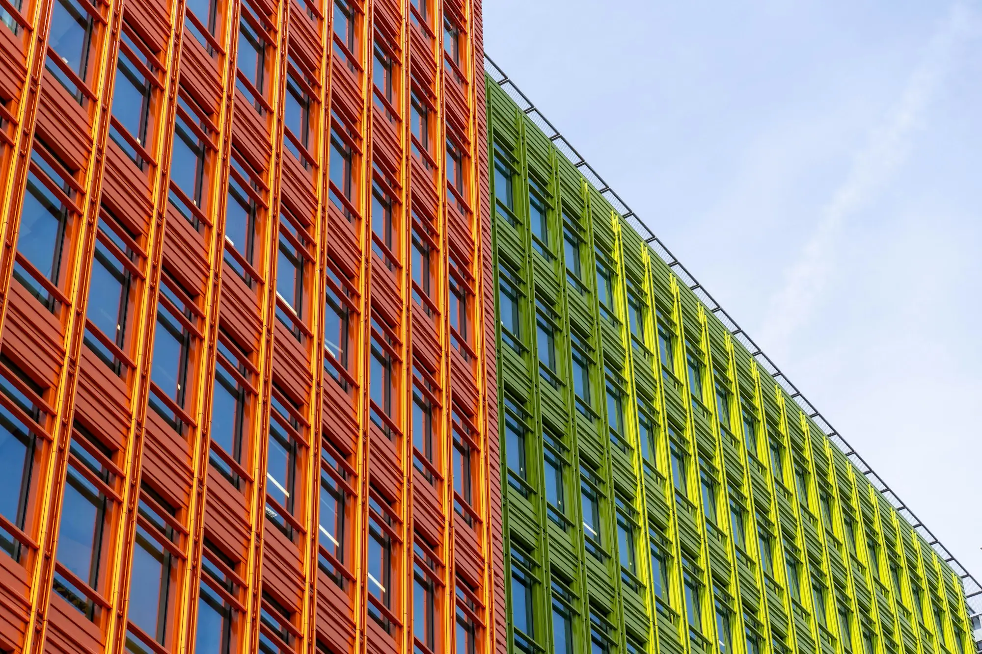 Modern commercial building facade with orange and green louvres against a blue sky